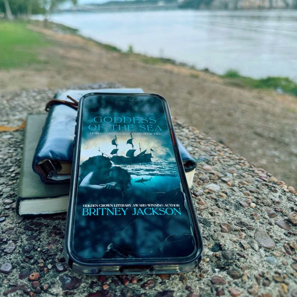 Goddess of the Sea (Lesbians, Pirates, & Dragons: Book 2) ebook, opened on a phone, with river in the background.